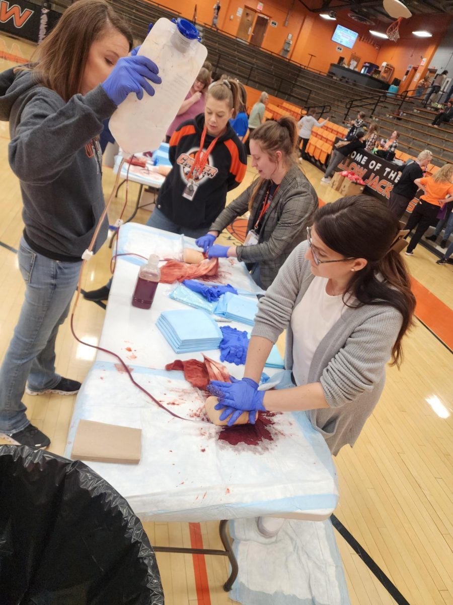 Ms. Hodge and Mrs Hammel practicing how to stop a deep wound from bleeding while Mrs. Ray looks on